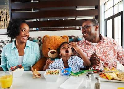 Smiling mother, father and son eating breakfast with large teddy bear