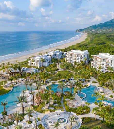 Aerial view of the pools and grounds at Conrad Punta de Mita with the ocean in the background.
