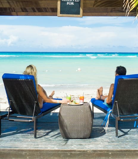 A couple sit under a cabana and look out to the ocean