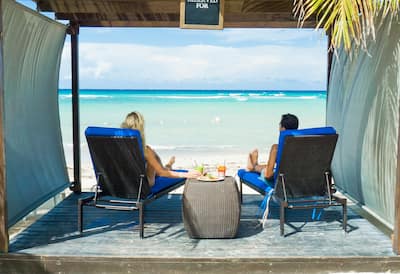 A couple sit under a cabana and look out to the ocean