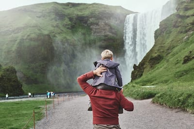 Family on vacation in Iceland. Father carries a small son on his shoulders to the famous waterfalls of Skogafoss.