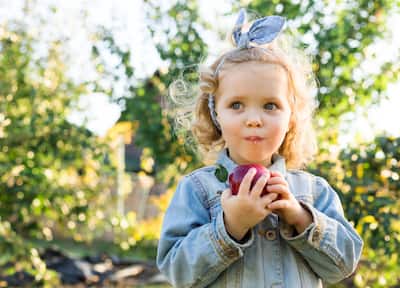 Little girl eating an apple with trees behind her.