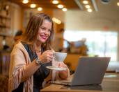 Woman holding a cup of coffee working on a laptop