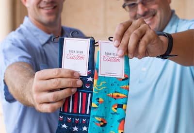 Two smiling men, each holding up a pair of colorful socks