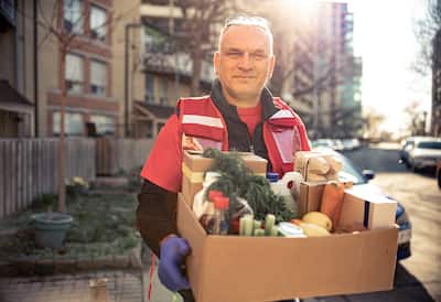 Delivery man holding box containing fresh vegetables, eggs, and bottled soda