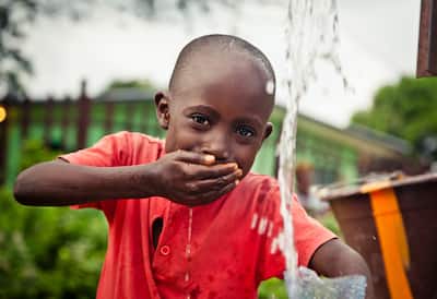 An African boy drinking water out of his hand from a water pump.