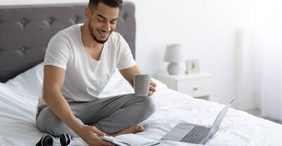 Young man in pajamas working on laptop in bed.