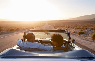Young African American couple smiling as they drive down a road in a convertible. 