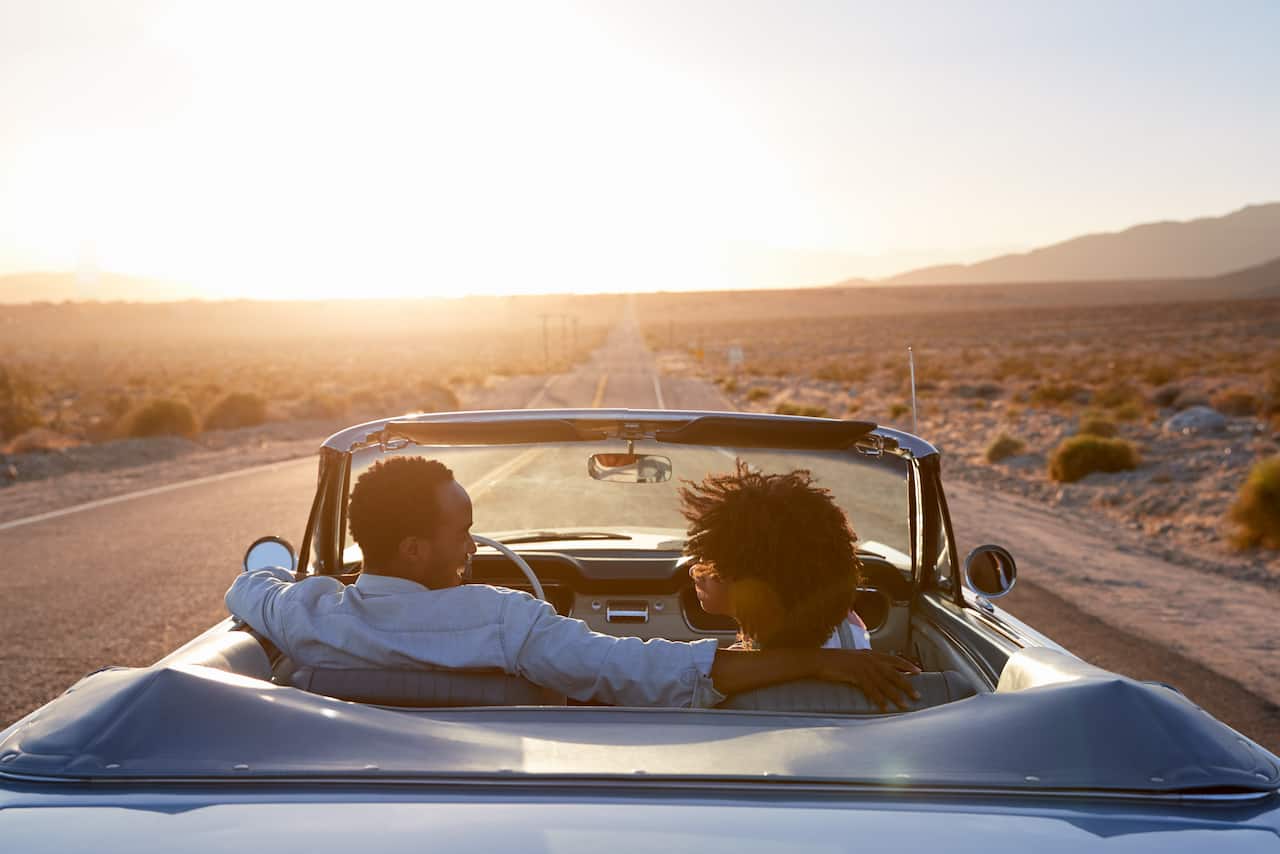 Young African American couple smiling as they drive down a road in a convertible. 