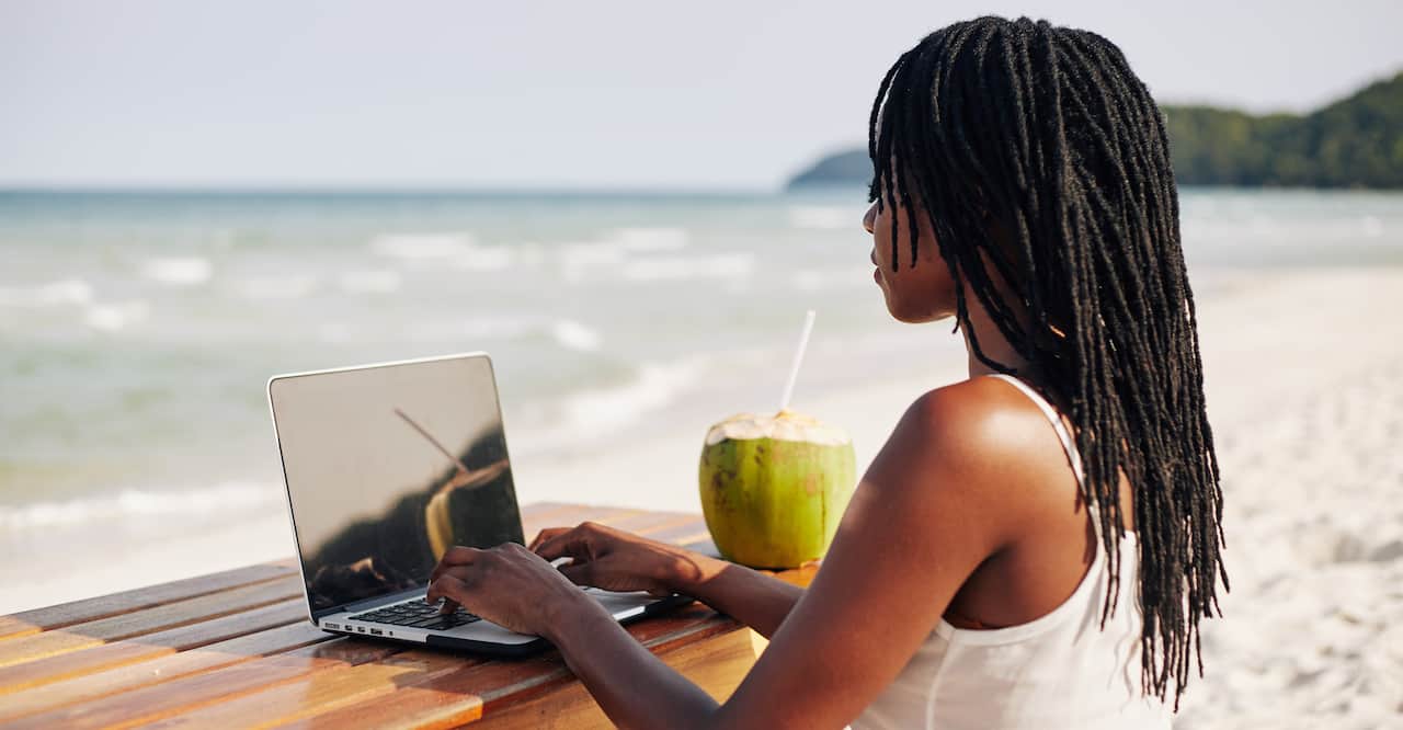 Young woman remotely working on laptop on the beach. 