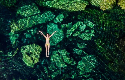 Overhead shot of a young woman in a bikini floating in the Cristalino cenote near Tulum, Mexico.