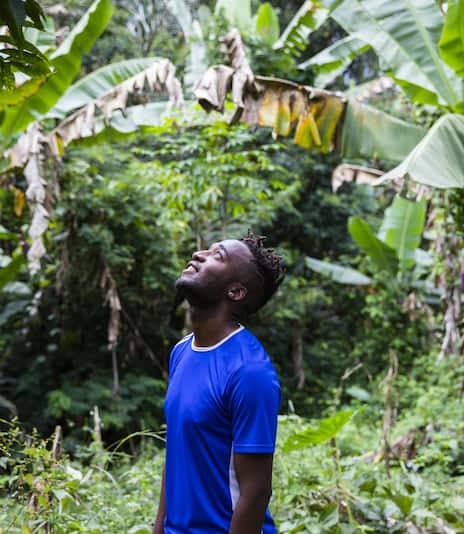 Young African American man looking up and smiling in the middle of a tropical jungle.