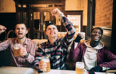 Happy male friends drinking beer and celebrating victory at bar or pub.