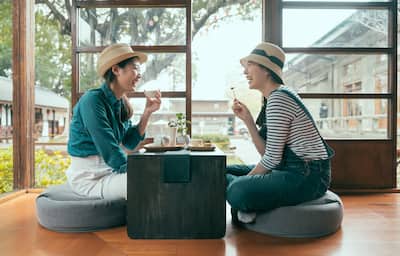 side view of two asian girls having fun laughing during afternoon tea time in local tea shop. Japanese style house Tokyo Japan. group of cheerful female friends enjoy local snack eating indoor