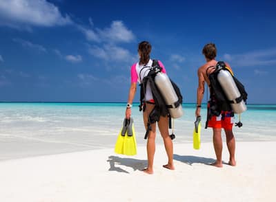 A man and a woman on a beach looking at the ocean and wearing scuba diving gear