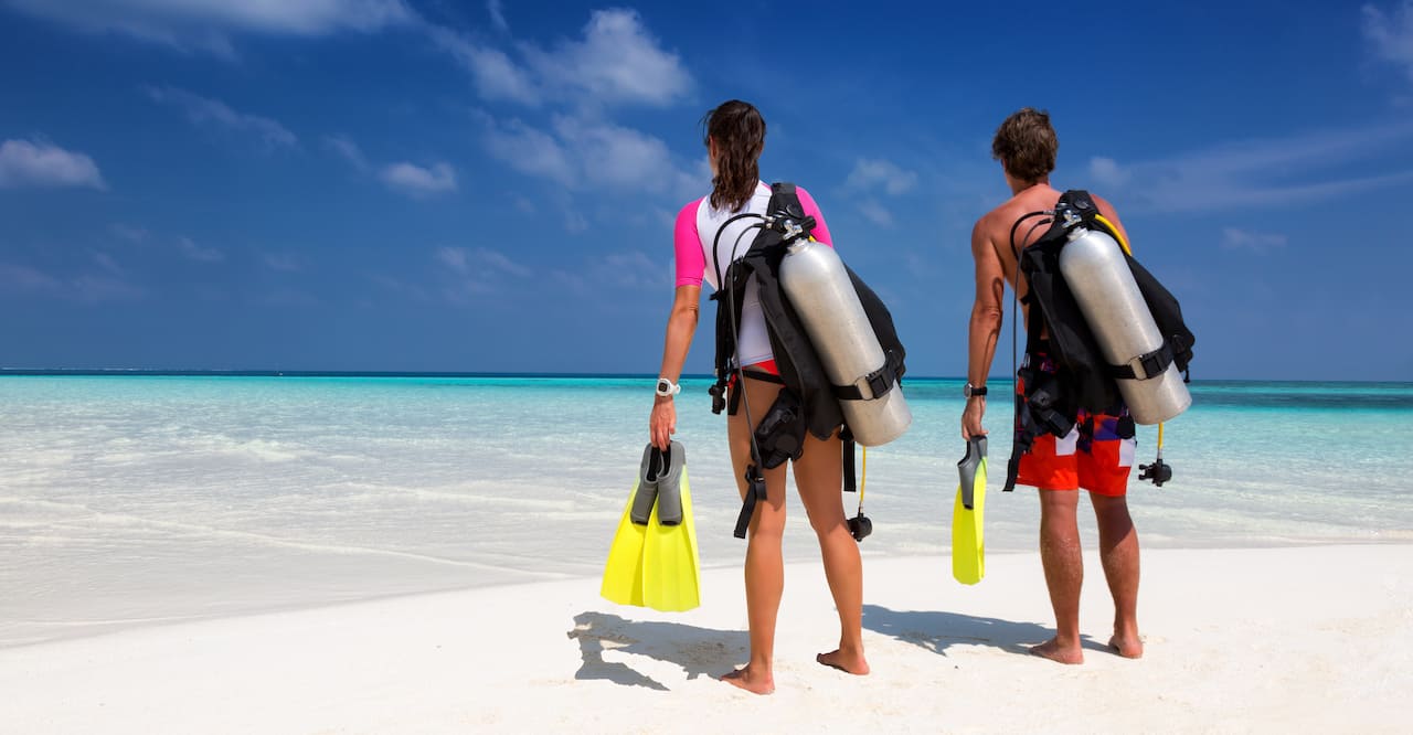 A man and a woman on a beach looking at the ocean and wearing scuba diving gear