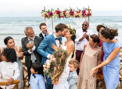 Wedding couple kissing in front of ocean and surrounded by wedding guests