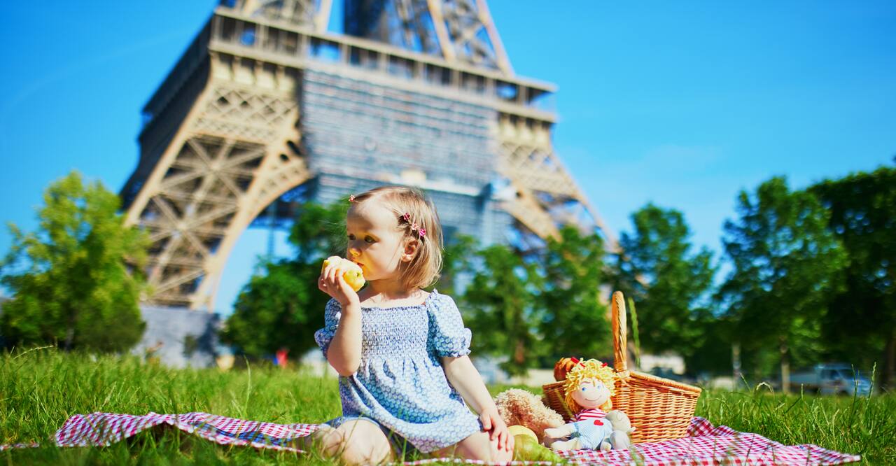 Cheerful toddler girl having picnic near the Eiffel tower in Paris, France. 