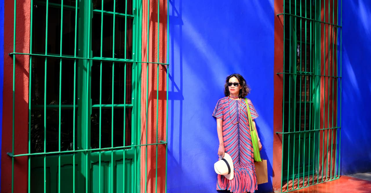 An Asian female tourist posing for a picture against the bright blue wall at Frida Kahlo Museum or Casa Azul in Coyoacán neighbourhood, Mexico City, Mexico.