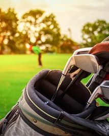 Detailed View of Golf Clubs in Bag and Golfer Putting On Golf Course in Background