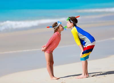 Little kids in rash guards for sun protection with snorkeling equipment on tropical beach having fun during summer vacation