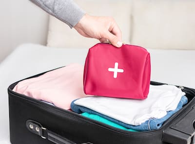 A person packing a suitcase on the trip with clothes and first aid kit.