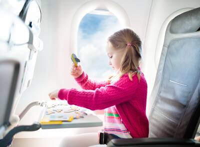 Kid in air plane sitting in window seat playing with a puzzle. 