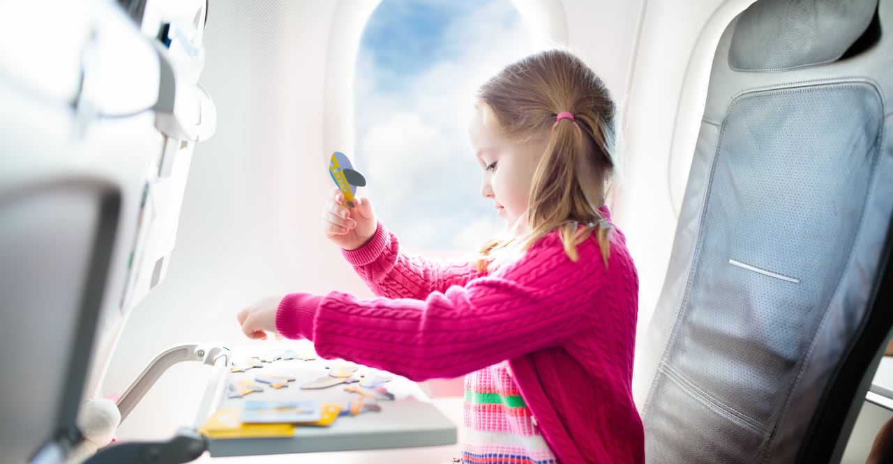 Kid in air plane sitting in window seat playing with a puzzle. 