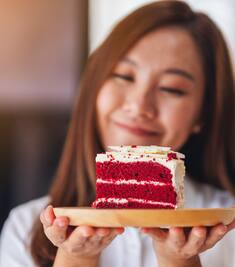 Closeup image of a young asian woman holding a piece of red velvet cake on wooden tray.