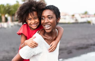 African American mom smiling and carrying her happy young daughter on her back.