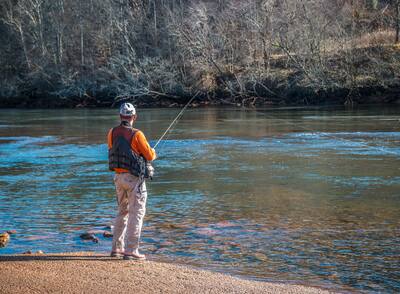 A man fishing at the boat ramp at the Chattahoochee river wearing a fishing vest waiting for a catch on a sunny day in winter