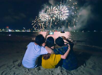Group of friends sitting and holding each others enjoy watching fireworks display on the beach.