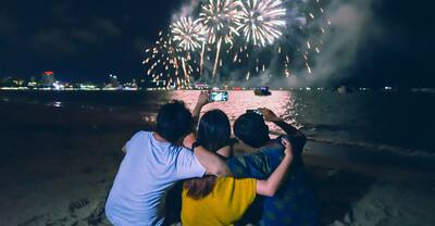Group of friends sitting and holding each others enjoy watching fireworks display on the beach.