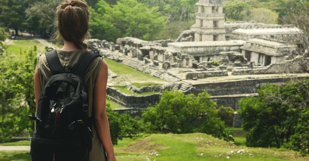 Hiker woman with backpack looking at ancient Mayan ruins