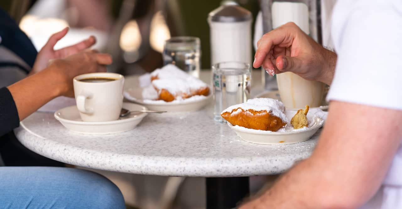 Two people enjoying beignets covered in powdered sugar.