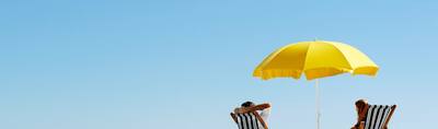 Two people under a yellow umbrella on the beach.