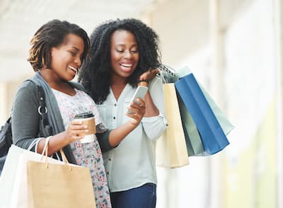 Happy African-American women reading message on smartphone while shopping.