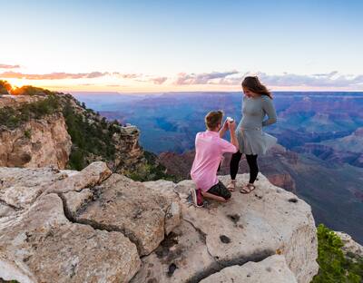 Man in pink shirt proposes to woman in black and white striped top next to the grand canyon