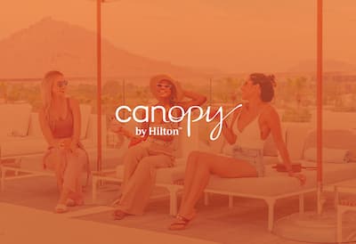 3 women laughing on loungers with the Canopy by Hilton logo on top of the image