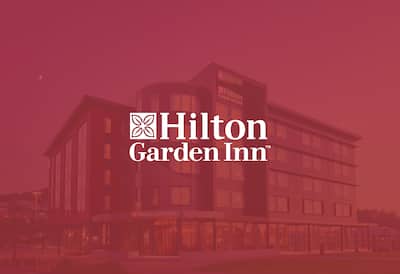 a hotel exterior with the Hilton Garden Inn logo layered over the top
