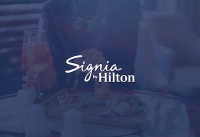  Woman holding fork and glass with the Signia by Hilton logo over the top of the image