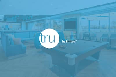 A hotel communal area with the Tru by Hilton logo layered over the top