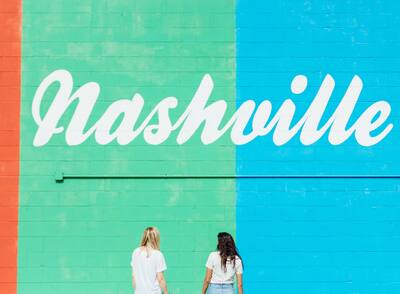 Two women looking at Nashville painted across a brick wall.
