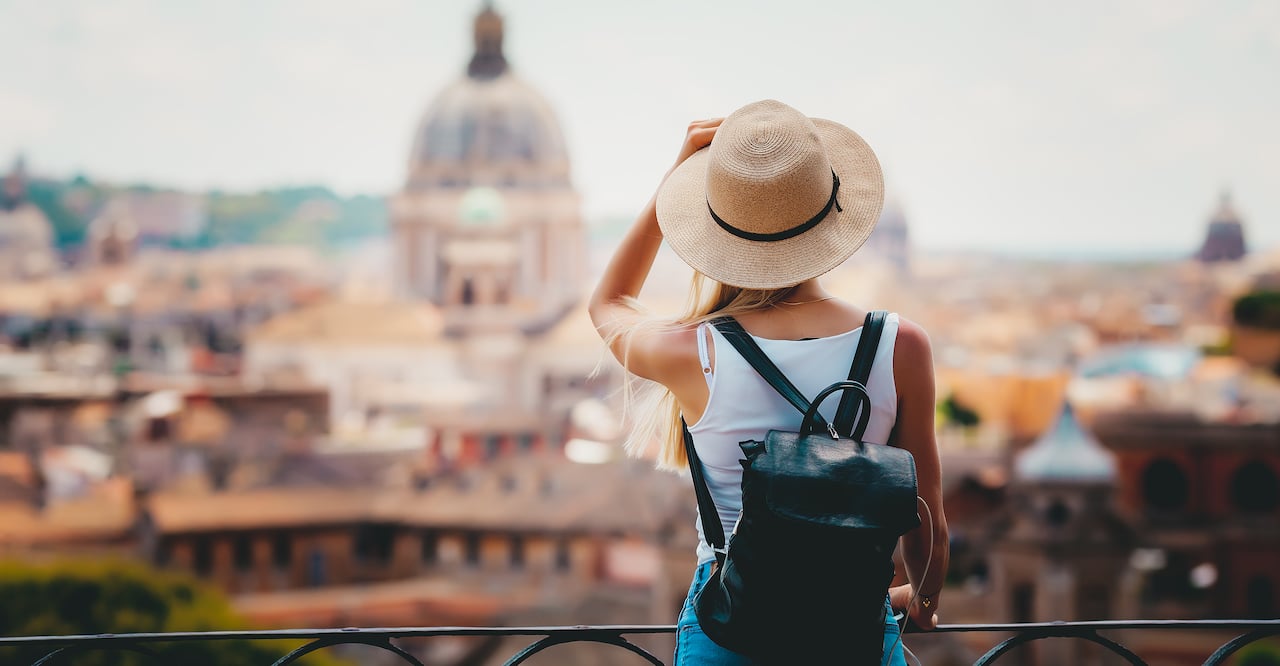 Young girl with mobile phone camera and map in hand standing on the hill looking on the cathedral Vatican.