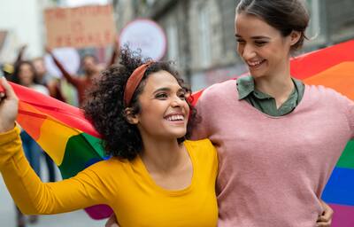 Young women on street enjoying holding a rainbow flag during a Pride parade.