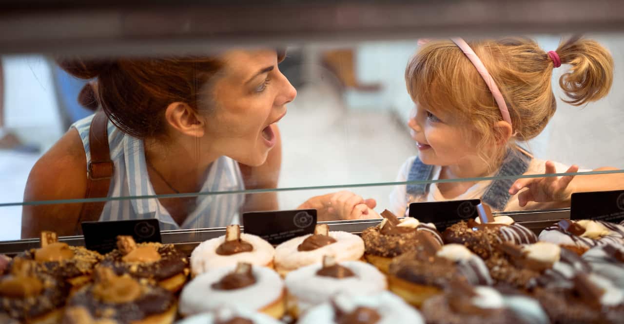 Lady and young girl look at each other next to donut display