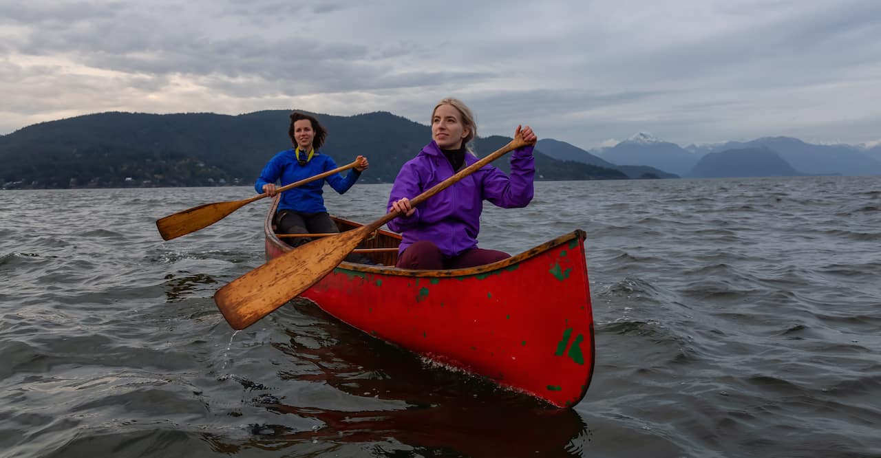 Female friends on a red canoe are paddling in the Howe Sound during a cloudy sunset. Taken in Horseshoe Bay, West Vancouver, BC, Canada.