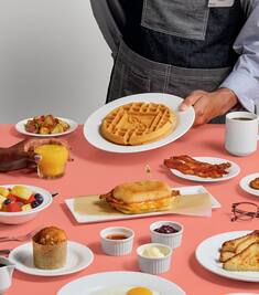 A waiter serving a selection of breakfast dishes on a pink table