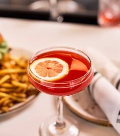 A close-up of a cocktail with food in the background