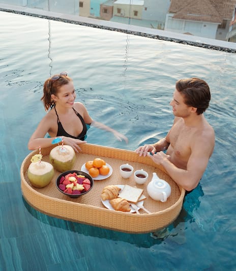 Couple in a pool with a floating tray with breakfast.